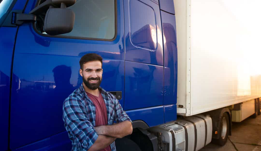 Man with cross arms smiling outside of 18 wheeler
